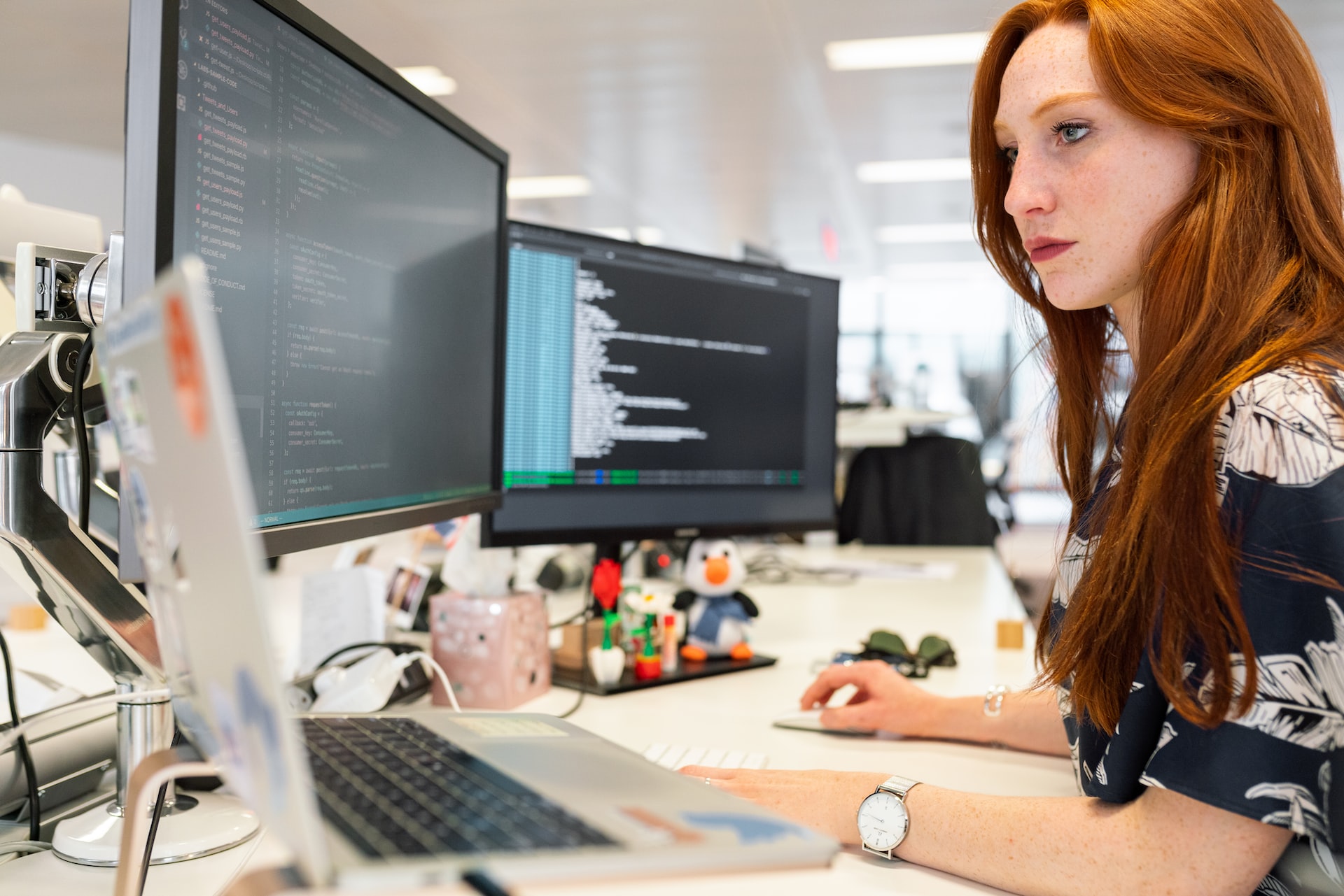 eine Frau schaut beim Programmieren konzentriert auf einen ihrer drei Monitore